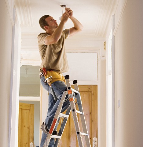 Man with toolbelt doing DIY at home, standing on step ladder, fixing light fixture in ceiling