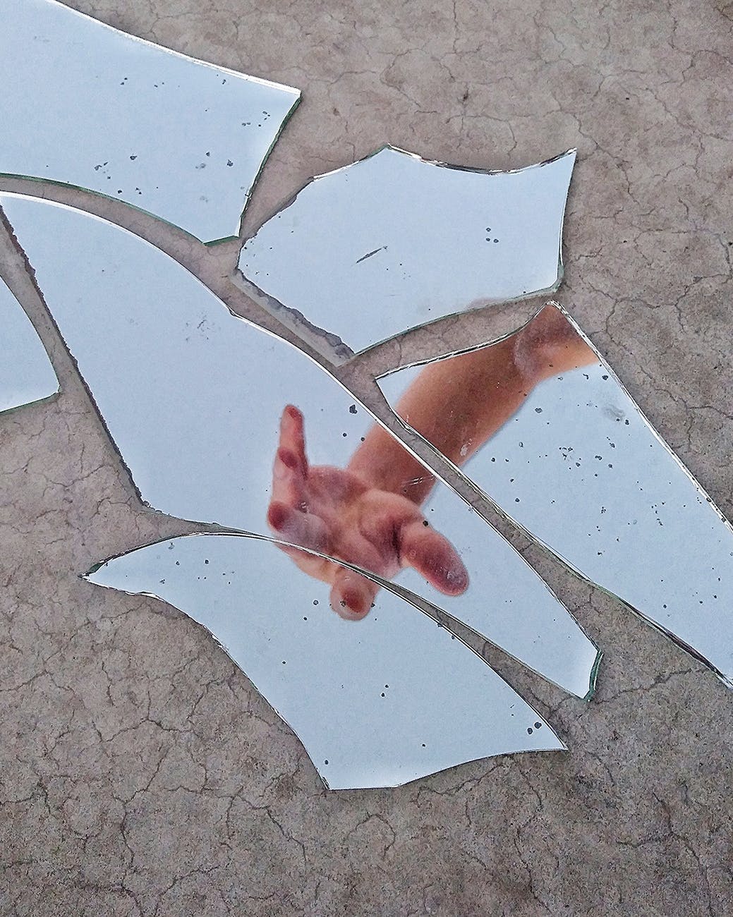 mirror fragments on gray surface with the reflection of a person s arm